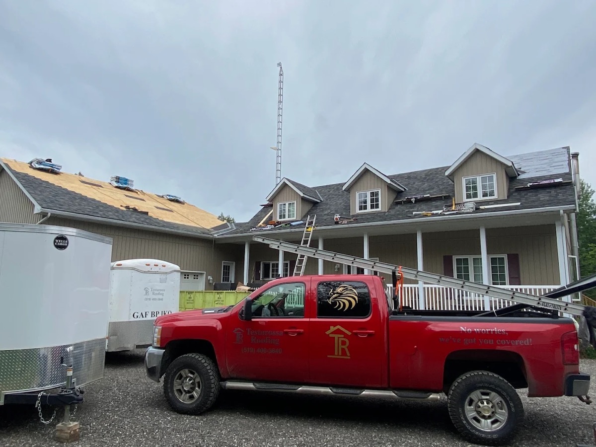 Red Testarossa Roofing pickup truck with logo decal, parked in front of a home mid re-roof