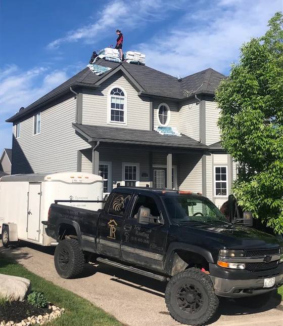 Testarossa Roofing truck and trailer in the driveway with a roofer on the ridge and shingle bundles staged across the roof