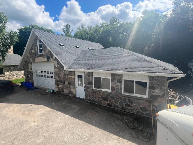 Stone garage and addition with a new charcoal shingle roof, fresh eavestrough and vents