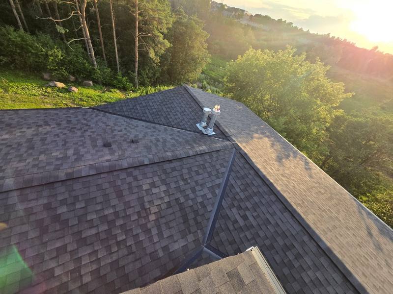 Finished shingle roof valley and hip at sunset with vents flashed in, view over the treeline