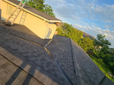 Finished charcoal shingle roof valley at sunset, ladder against the gable wall