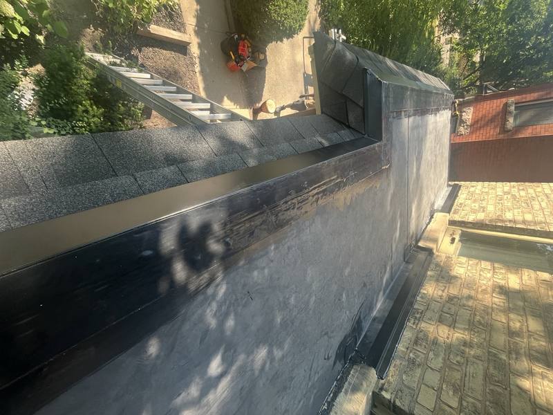 Close-up of a flat roof parapet wall with fresh membrane and metal flashing, ladder set up below