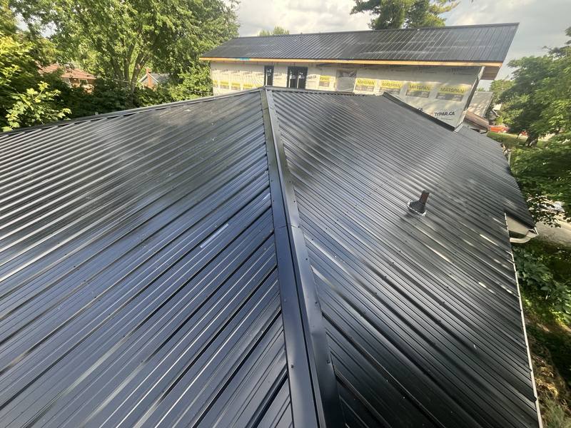 Finished black standing seam metal roof on a home mid-renovation, ridge caps and panels running clean to the eaves