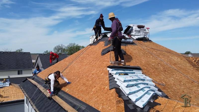 Two Testarossa roofers working the ridge of a stripped roof, deck exposed and new bundles staged behind them