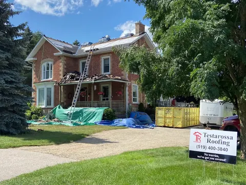 Roof tear-off in progress on a red brick Victorian home, old shingles stripped to the deck