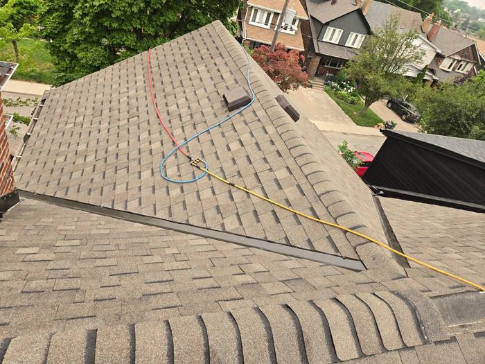 Aerial view of a finished shingle roof meeting a low-slope flat section, with new metal transition flashing run along the join and roof vents set in