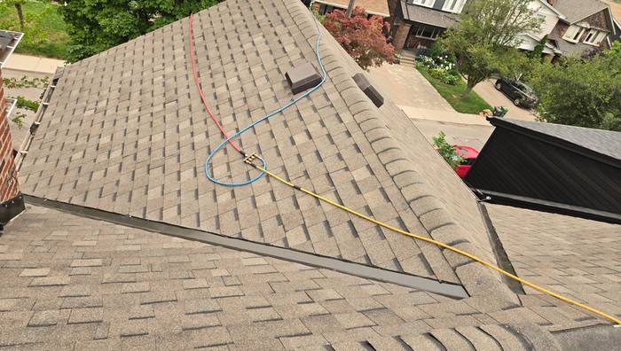 Aerial view of a finished shingle roof meeting a low-slope flat section, with new metal transition flashing run along the join and roof vents set in