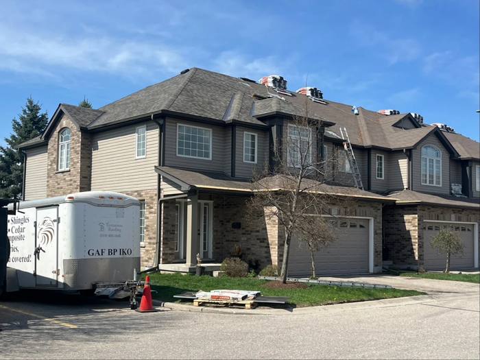 Testarossa Roofing crew re-roofing a townhouse block, shingle bundles staged along the ridge and the company trailer parked at the curb