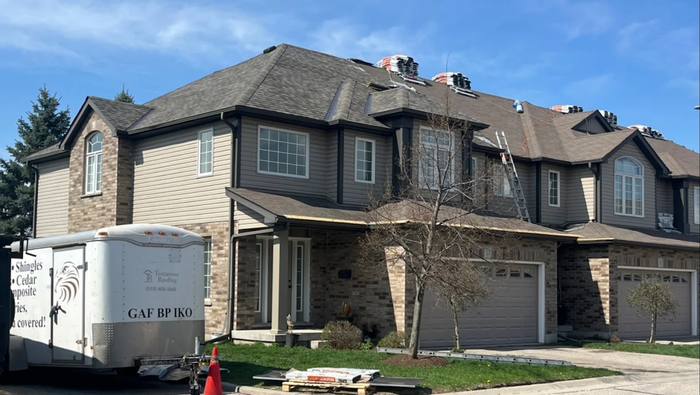 Testarossa Roofing crew re-roofing a townhouse block, shingle bundles staged along the ridge and the company trailer parked at the curb