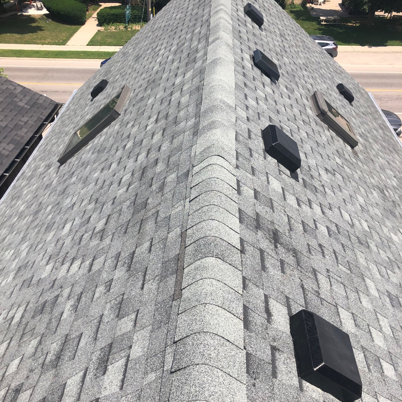 Close-up of architectural shingles with vent stacks and skylight housings on a roof ridge